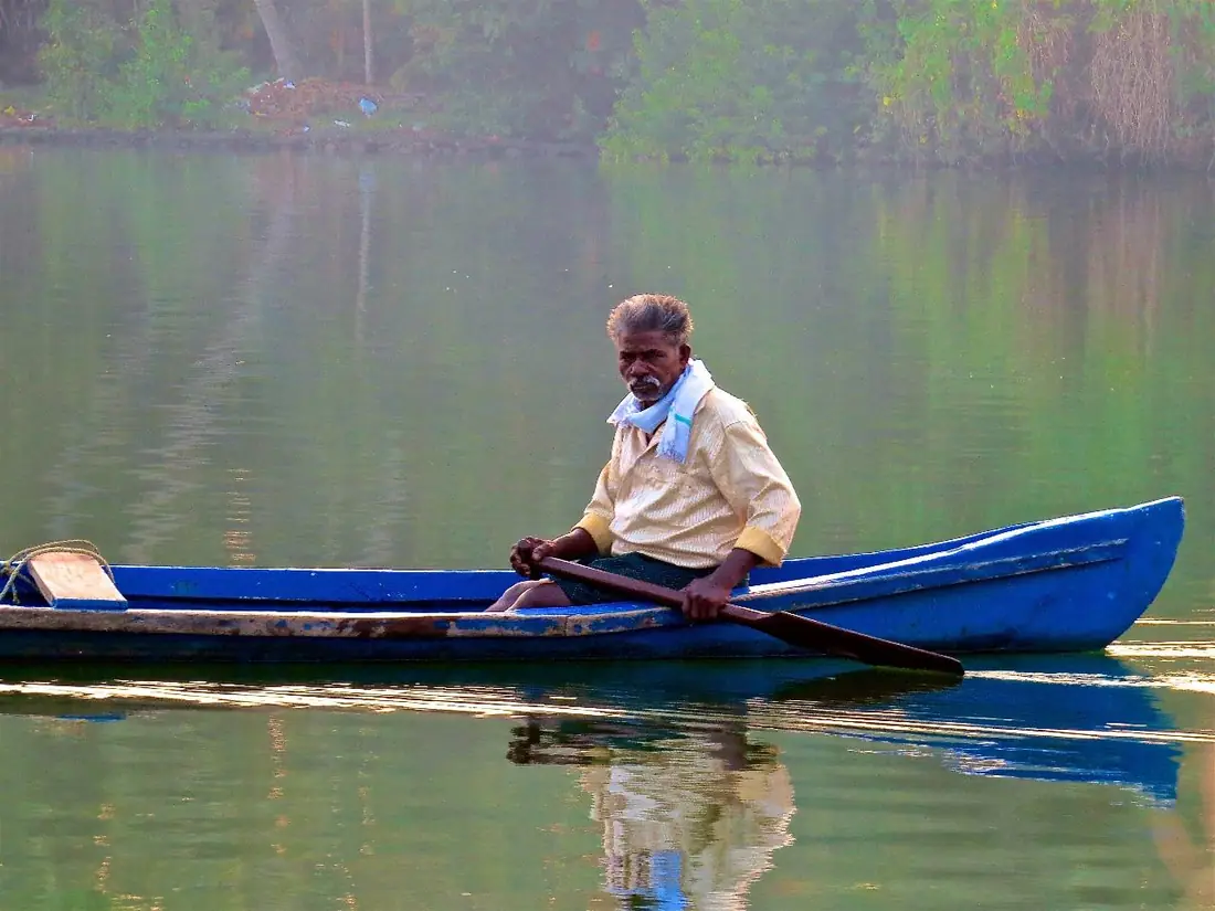 Barqueiro remando numa canoa azul em água calma