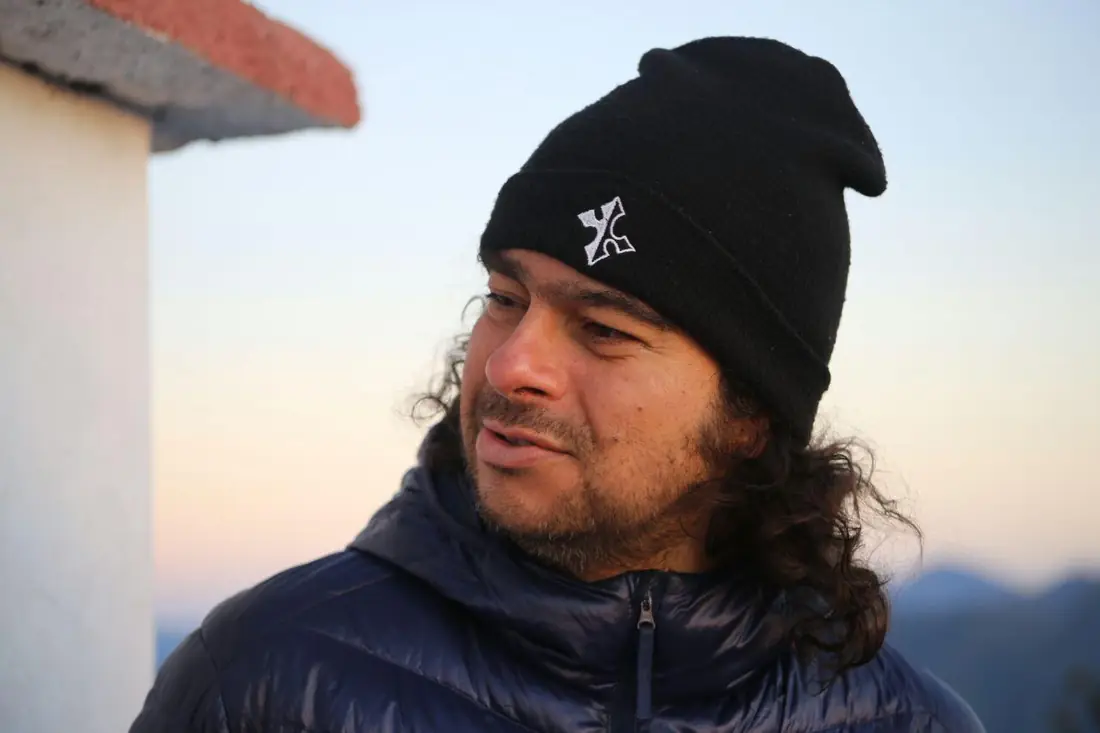 Homem de gorro preto e cabelo comprido, com o céu claro do amanhecer ao fundo